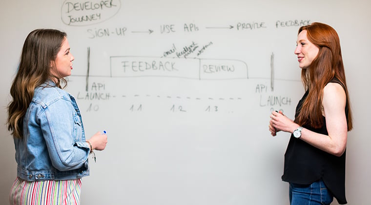 Two people standing in front of a white board looking at job data