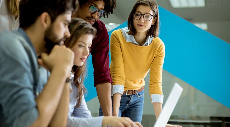 A group of HR Tech employees gathers around a computer desk to discuss their industry's top challenges. 