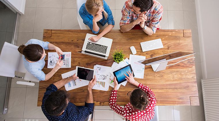 Five coworkers sit at a conference table with their computers.