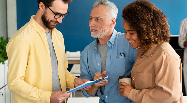 Three co-workers discussing document on clipboard